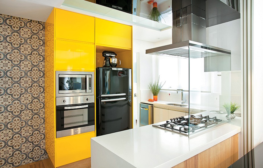 O armário de laca brilhante e amarela deu ar moderno à cozinha que é aberta para a sala. A cor divertida é equilibrada com o aço inox e o preto dos eletrodomésticos