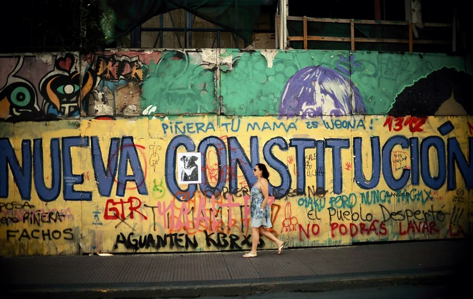 Mulher passa por um grafite que pede uma nova Constituição em Santiago, no Chile