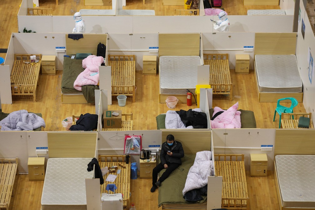 5 de março - Médicos (na parte de cima da imagem) passam por camas vazias enquanto um paciente descansa em um hospital temporário criado para pacientes com o novo coronavírus COVID-19 em um estádio de esportes em Wuhan, na província central de Hubei, na China — Foto: AFP
