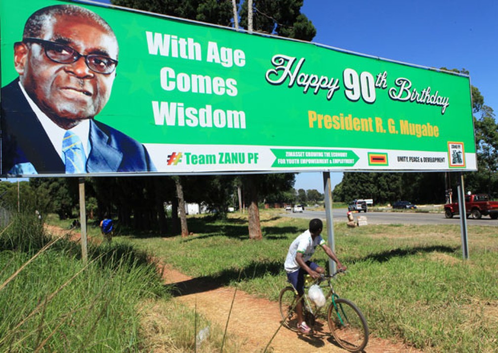 Homem passa de bicicleta em frente a outdoor de aniversário dos 90 anos de Robert Mugabe.  — Foto: Tsvangirayi Mukwazhi / AP Photo