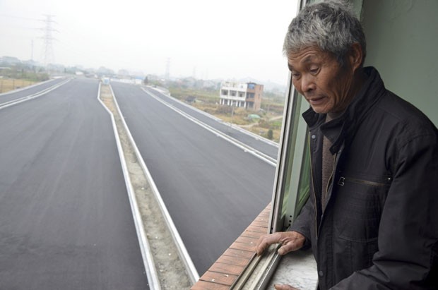 Idoso observa da janela estrada contornando sua casa. (Foto: China Daily/Reuters)