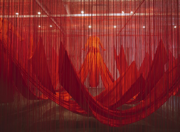 Grandiosa, a instalação de Chiharu Shiota é composta por três grandes vestidos vermelhos, além de cerca de 10 mil fios pendurados verticalmente, totalizando mais de 34 quilômetros de material (Foto: Divulgação )