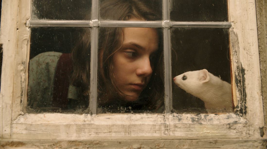 A protagonista, Lyra Belacqua ( a atriz Dafne Keen),  tem como “dimon”, Pantalaimon, que assume de vez em quando a forma desse rato felpudo  (Foto: Divulgação/ HBO )