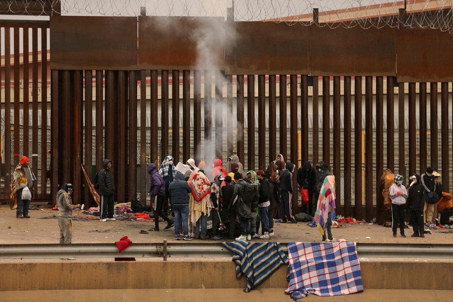 Imigrantes se aquecem junto a fogueira no muro que separa os EUA do México em Ciudad Juárez