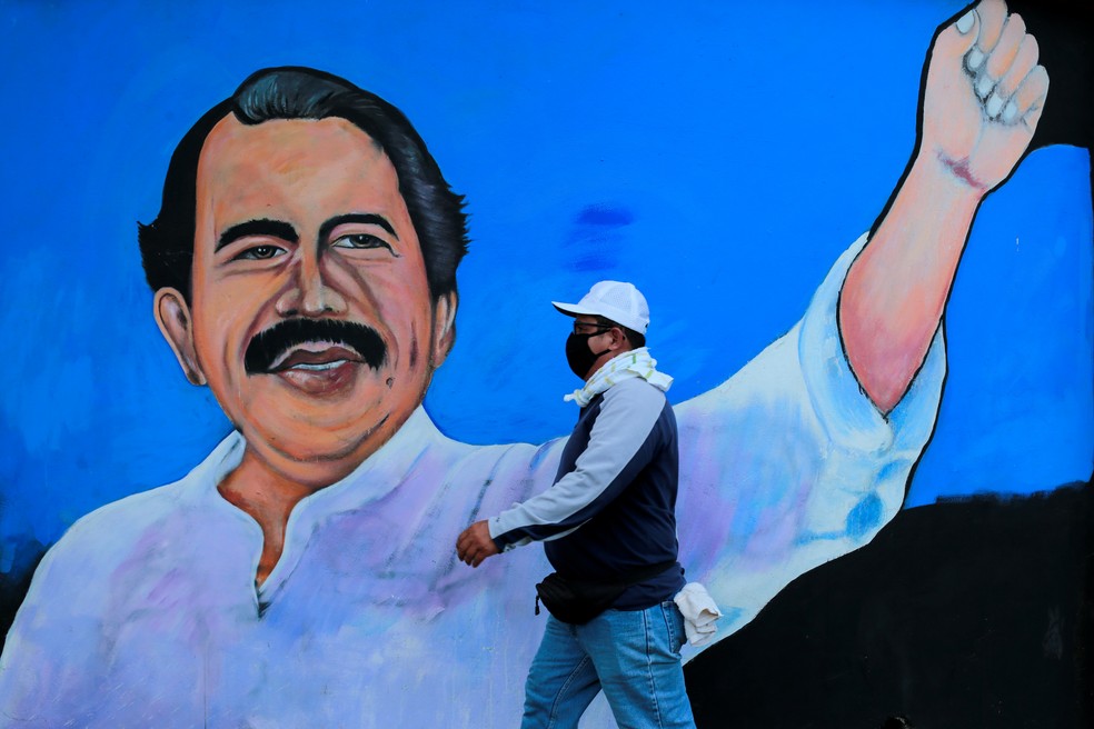 Homem com máscara caminha em frente a um muro com a figura do presidente da Nicarágua, Daniel Ortega, em 30 de março — Foto: Oswaldo Rivas / Reuters
