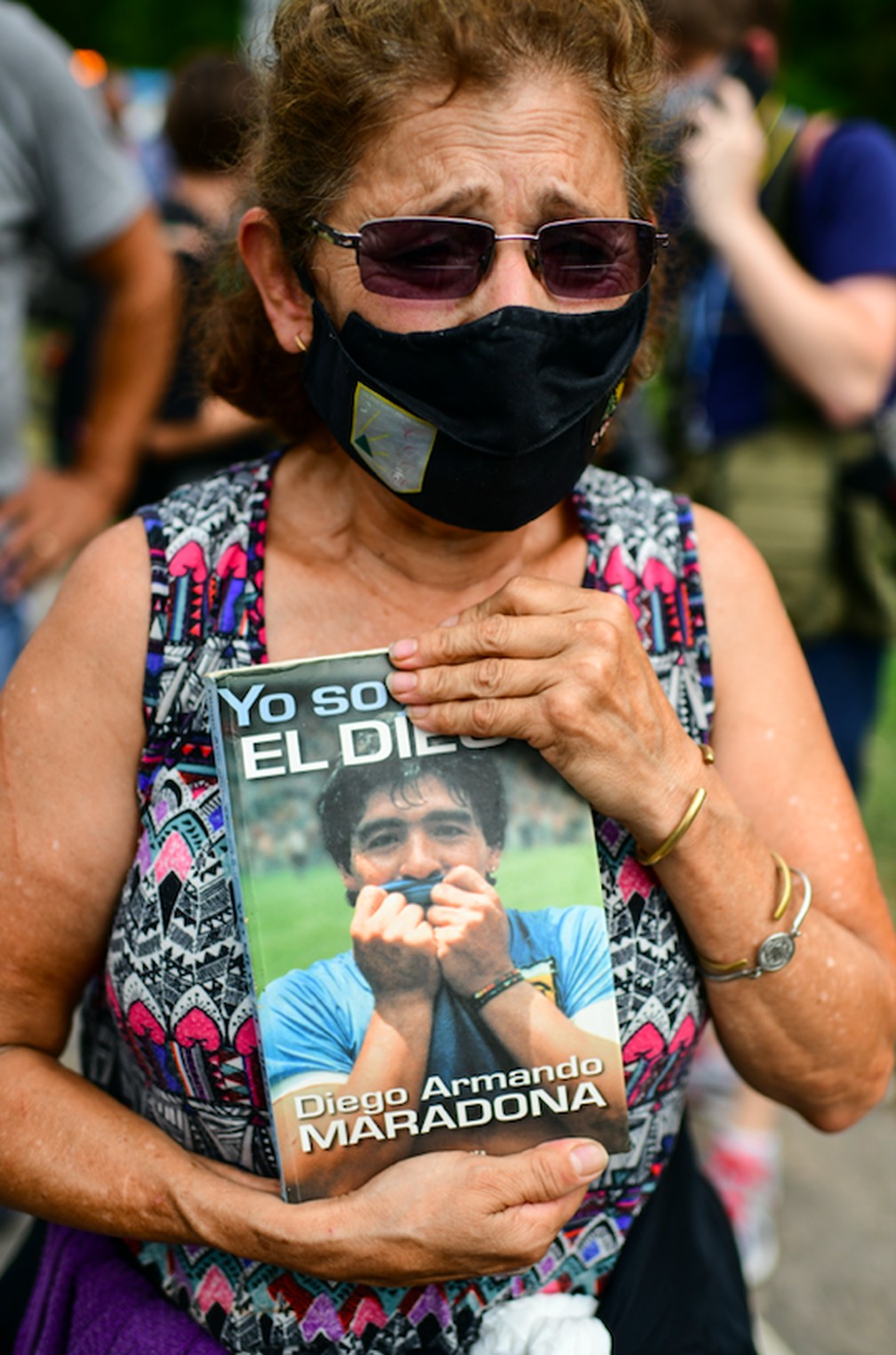 Mulher segura um livro com a foto de Diego Maradona do lado de fora do condomínio onde o astro do futebol argentino morreu nesta quarta-feira (25) na região metropolitana de Buenos Aires — Foto: Ronaldo Schemidt/AFP