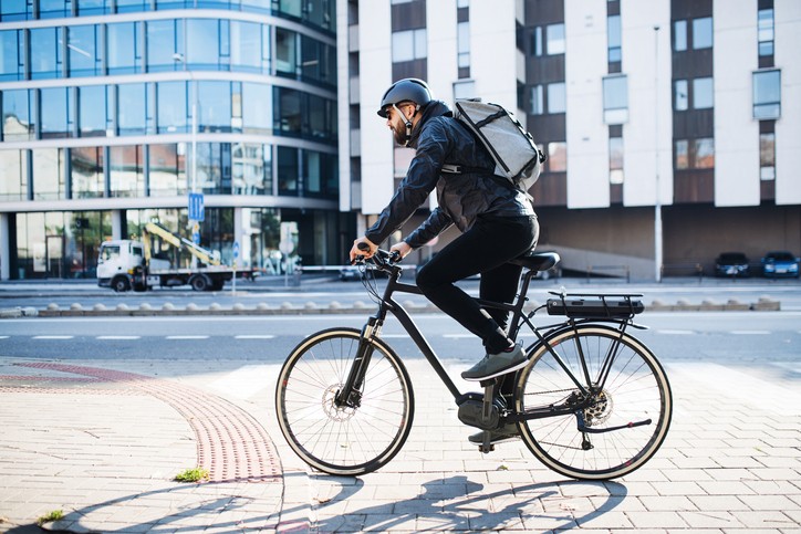 Male hipster courier with bicycle cycling on a road in city, delivering packages. Copy space. (Foto: Getty Images/iStockphoto)