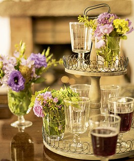O prato de doces com dois andares virou porta-copos para as taças de vinho e suporte para os pequenos arranjos de flores