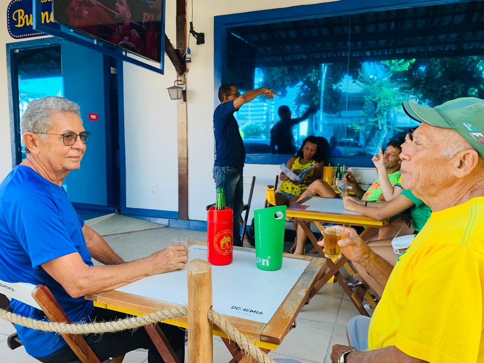 Davino Tenório (de amarelo) e o amigo Bezerra (de azul) se reuniram em um bar em Maceió para assistir ao jogo do Brasil na Copa do Mundo — Foto: Vivi Leão/g1