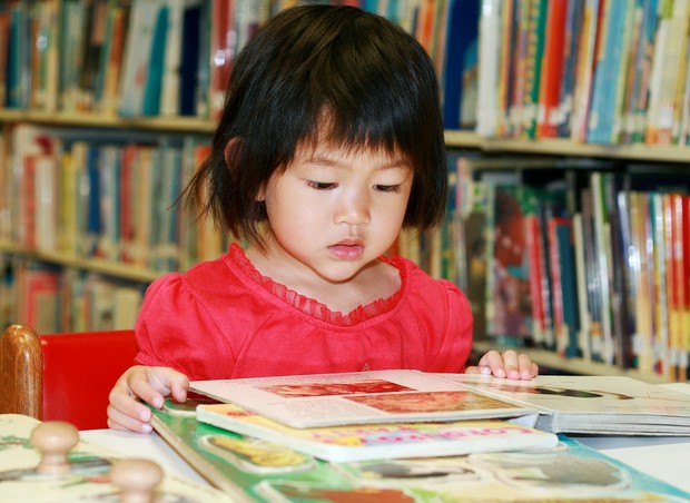 Criança lendo livros sozinha na biblioteca da escola (Foto: Shutterstock)