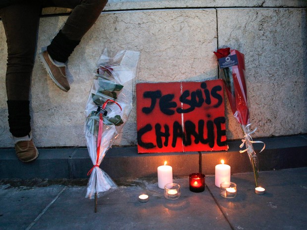Flores, velas e um cartaz escrito 'Eu sou Charlie' são vistos próximos a um muro durante uma manifestação em Paris. Três homens armados e mascarados invadiram a redação da Charlie Hebdo matando 12 pessoas, incluindo o seu editor, antes de fugir (Foto: Christophe Ena/AP)