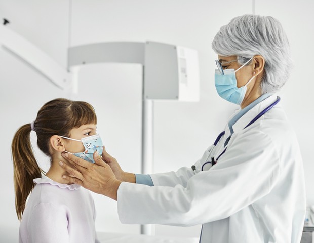 Mature female pediatrician examining patient. Healthcare worker is touching throat of girl in examination room. They are at hospital during COVID-19 outbreak. (Foto: Getty Images)