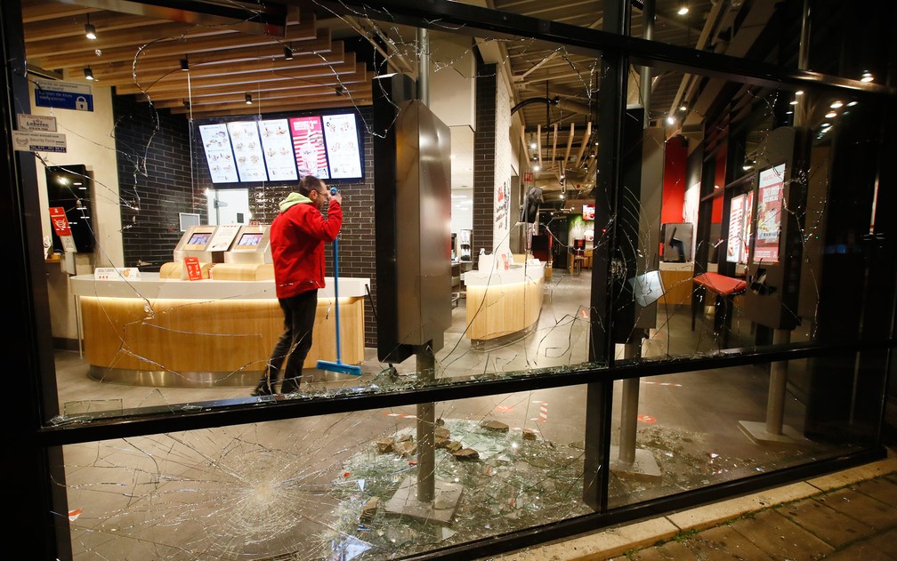 Homem limpa restaurante de fast food com janelas quebradas durante protesto contra toque de recolher em Roterdã, na Holanda, na segunda-feira (25) — Foto: AP Photo/Peter Dejong