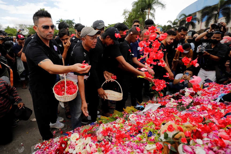 Jogadores e funcionários do Arema FC colocam pétalas em um monumento às vítimas da tragédia no estádio Kanjuruhan na Indonésia — Foto: REUTERS/Willy Kurniawan