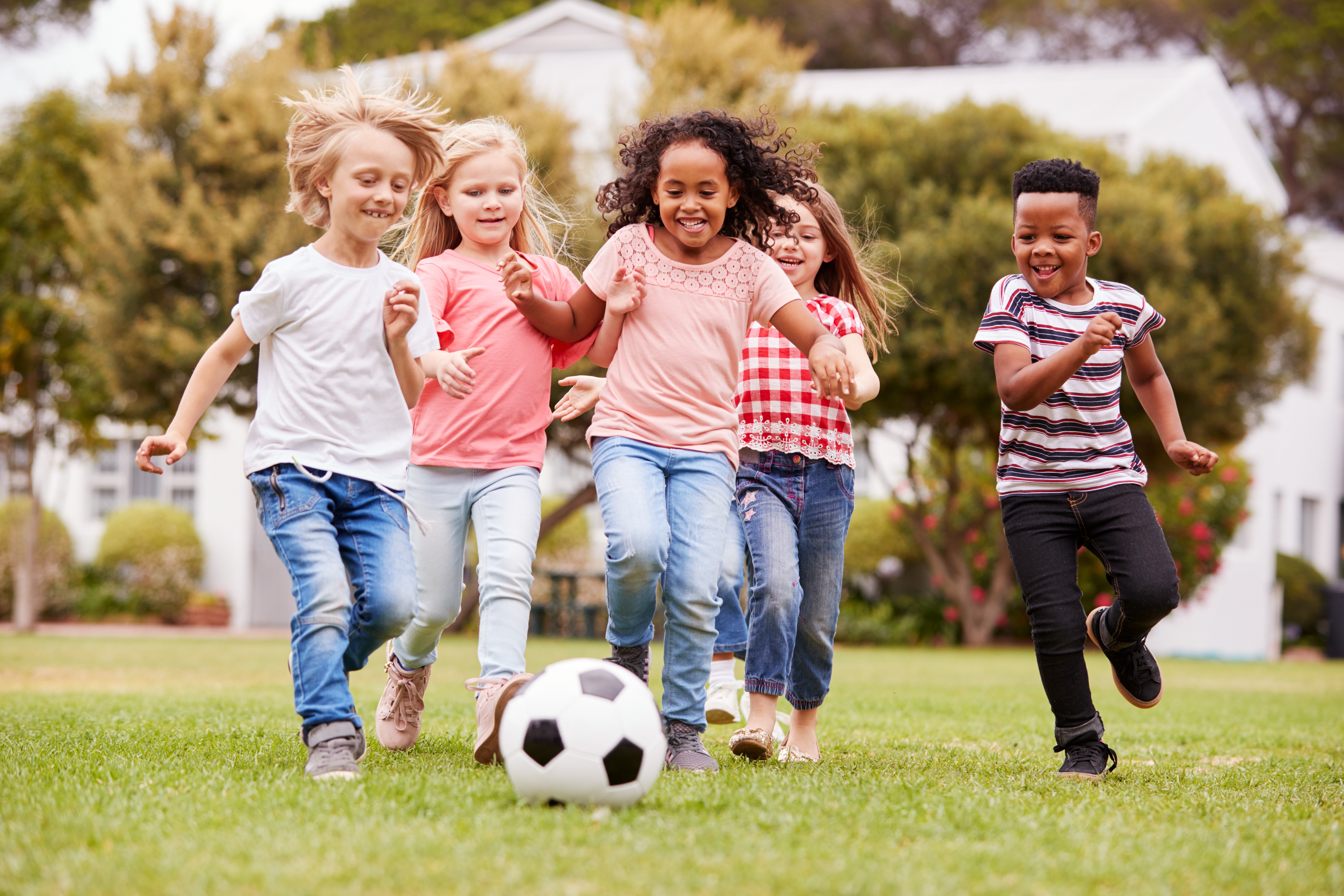  A group of children are playing soccer together outside and smiling.