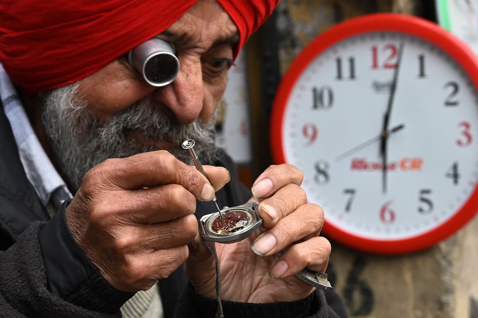 Relojoeiro trabalha em sua banca ao longo de uma rua em Amritsar, Índia — Foto: NARINDER NANU/AFP