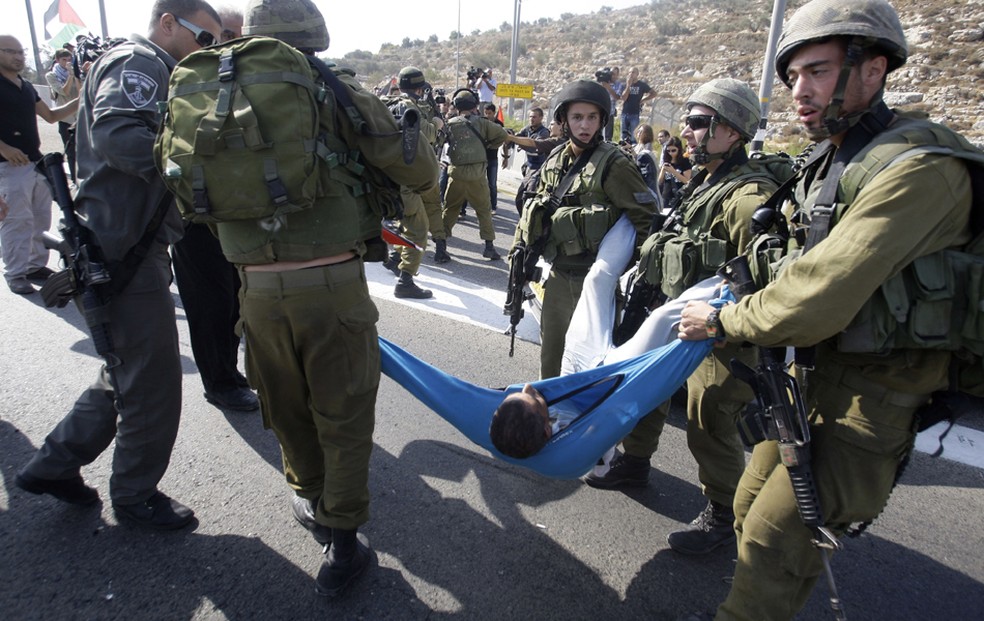 Soldados israelenses carregam um palestino ferido em briga durante um protesto na estrada 443, perto da aldeia de Beit Ur, na Cisjordânia. Palestinos bloquearam a estrada para protestar contra ataques dos colonos judeus dos palestinos em suas propriedades (Foto: Nasser Shiyoukhi/AP)