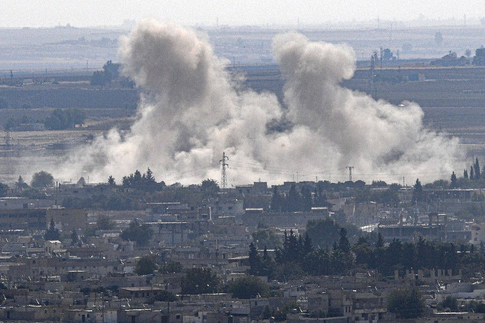 Uma nuvem de fumaça é vista na cidade síria de Ras al-Ain, do lado turco da fronteira em Ceylanpinar, no distrito de Sanliurfa, na primeira semana de operação militar turca contra as forças curdas — Foto: Ozan Kose/AFP
