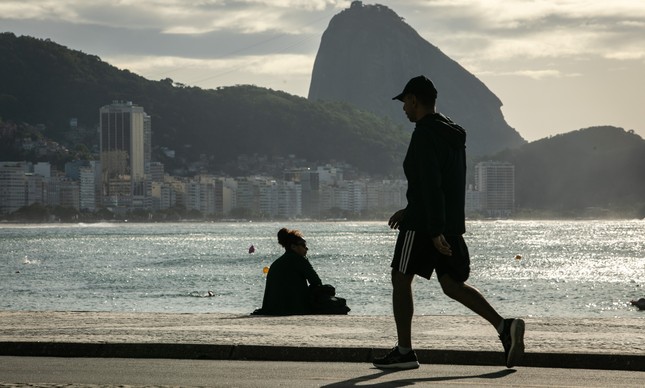Homem caminha na orla de Copacabana.