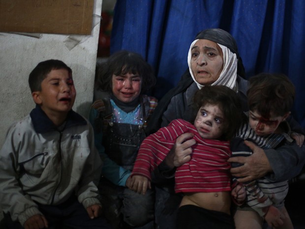 Uma mulher acompanha crianças que aguardam atendimento em uma clínica improvisada na região de Douma, na Síria, após ataques aéreos das forças do governo, no domingo (15) (Foto: AFP Photo/Abd Doumany)