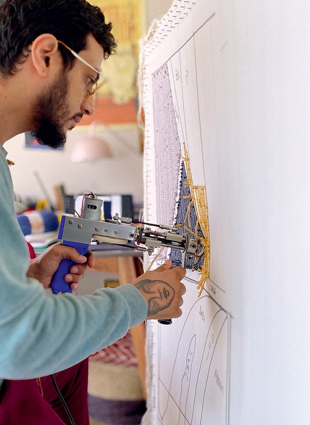 Alex usa uma pistola para aplicar os fios de lã na tela com o desenho que serve de base para a tapeçaria (Foto: Divulgação)