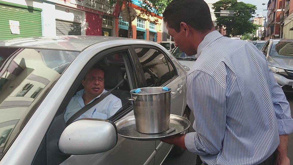 Como um garçom, ele oferece água e suco em uma bandeja no meio dos carros em Bauru (Foto: Alan Schneider / TV TEM )