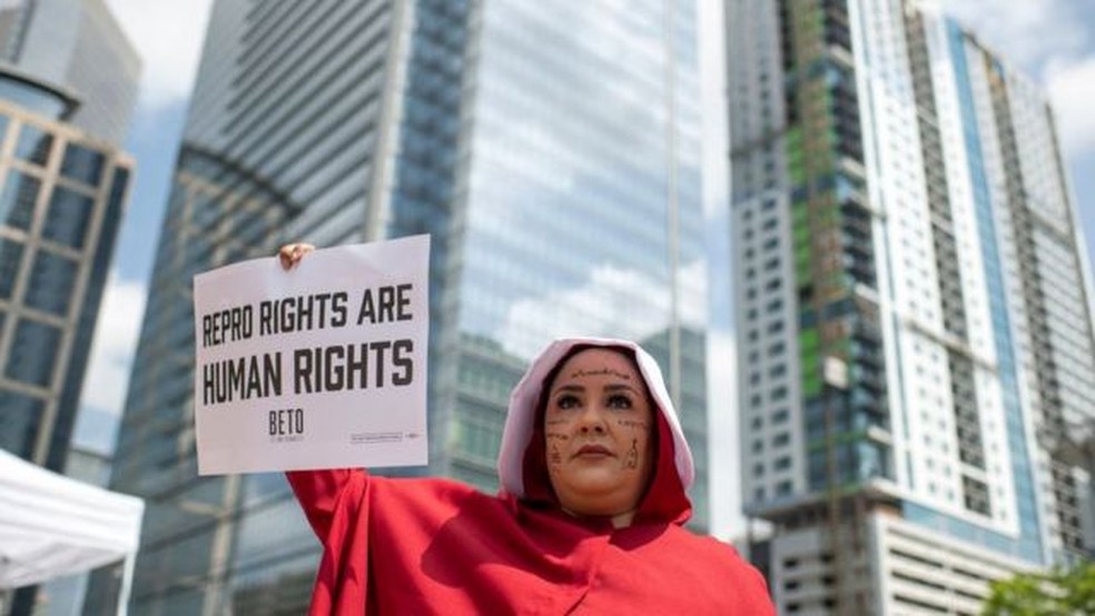 Direitos reprodutivos são direitos humanos, diz cartaz de manifestante a favor do direito de abortar vestida como personagem de " O Conto da Aia" — Foto: BBC