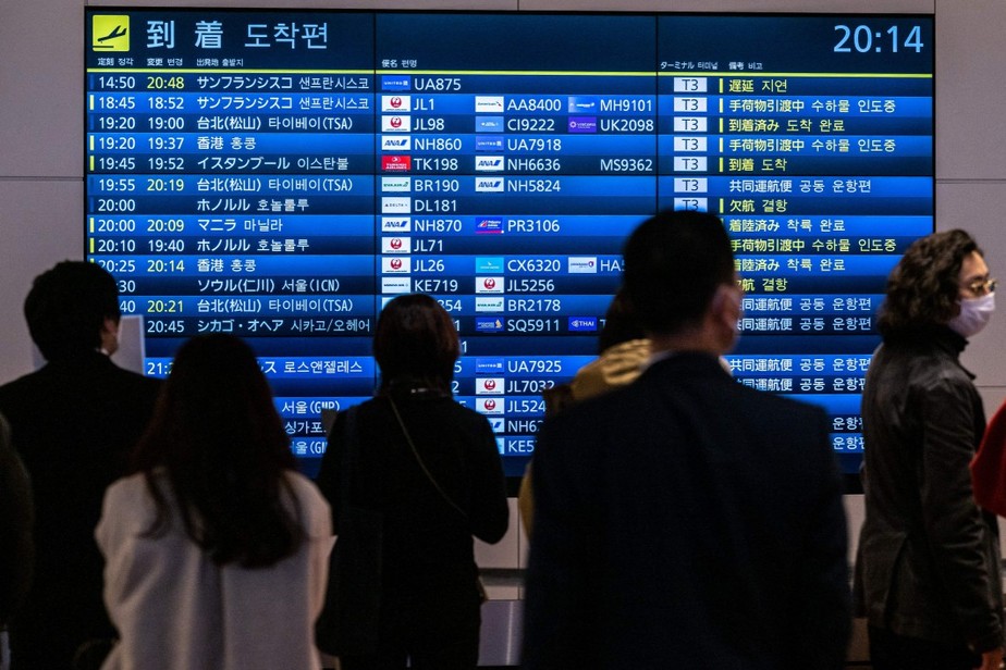 Passageiros observam painel no Aeroporto Internacional Haneda em Tóquio, no Japão