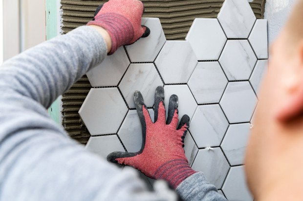 tiling - man laying marble texture hexagon tiles on the wall (Foto: Getty Images/iStockphoto)