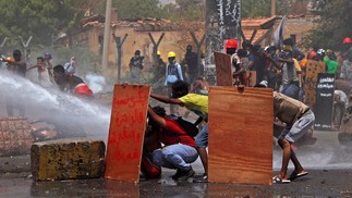 Manifestantes se protegem enquanto a tropa de choque tenta dispersá-los com canhões de água durante uma protesto contra o regime militar no centro da capital do Sudão, Cartum — Foto: AFP