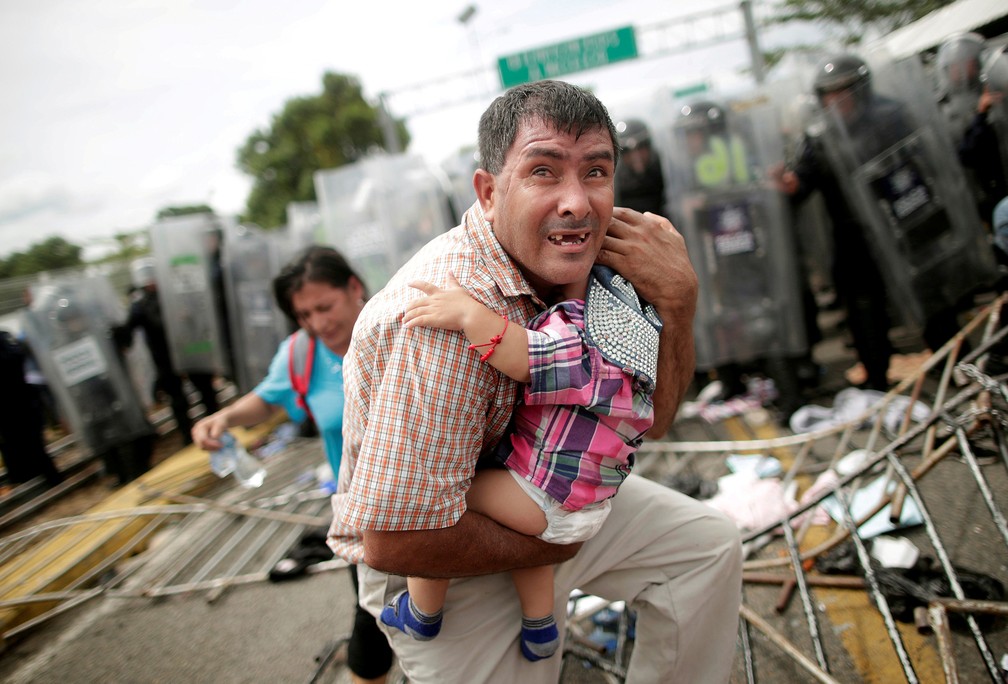 Um migrante hondurenho protege o filho depois que outros migrantes, parte de uma caravana, invadiram um posto fronteiriço em Ciudad Hidalgo, no México — Foto: Ueslei Marcelino/Reuters