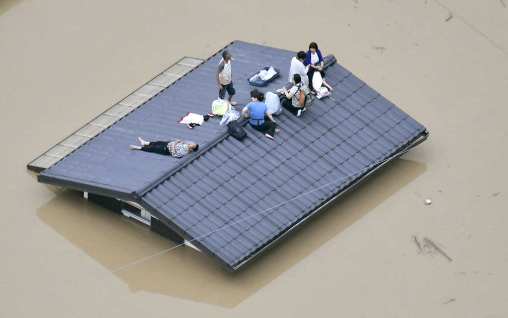 Vista aérea mostra moradores sobre telhado da casa submersa em uma área inundada em Kurashiki, sul do Japão (Foto: Kyodo / via Reuters)
