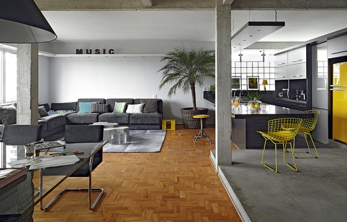 A cozinha é totalmente integrada à sala no apartamento do arquiteto Diogo Oliva. Os espaços são delimitados apenas pelo piso: tacos na parte social e cimento queimado e pastilhas pretas nas áreas molhadas. O amarelo quebra a seriedade da decoração