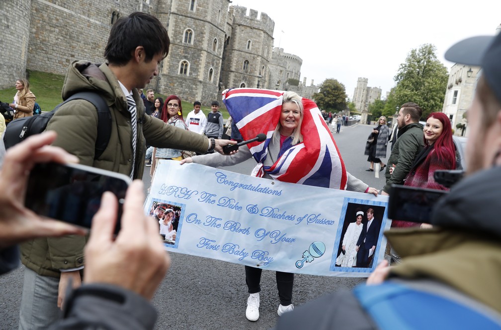 Fã carregando um cartaz parabenizando Meghan e Harry é entrevistada na segunda-feira (6), dia do nascimento do bebê. — Foto: Alastair Grant/AP