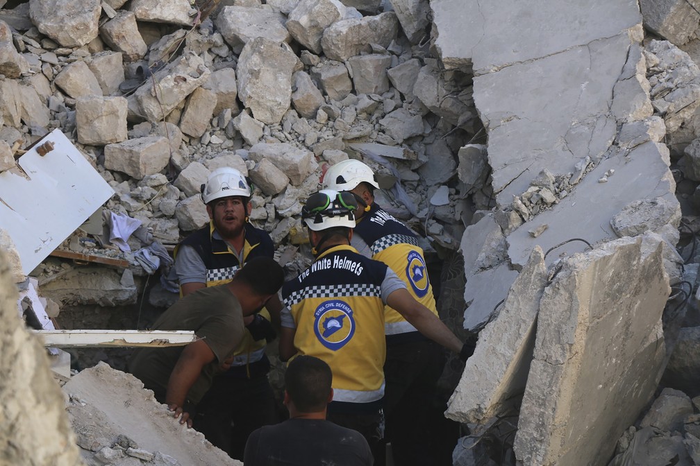 Membros dos Capacetes Brancos da Síria procuram vítimas em prédio destruído por ataques nesta segunda-feira (22), supostamente realizados pelo governo sírio ou pela Rússia. — Foto: Syrian Civil Defense White Helmets via AP