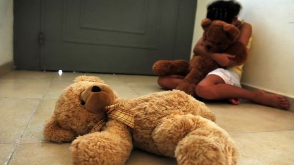 Criança abraçada com urso de pelúcia sentada no chão — Foto: Getty Images