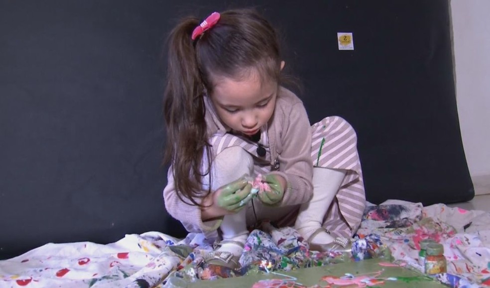 Manu pintas os quadros com as mãos misturando as tintas de variadas cores  — Foto: TV TEM / Reprodução