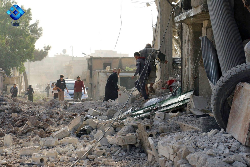 Sírios caminham sobre os destroços de mercado em Atareb, na Síria.  (Foto: Thiqa News via AP)