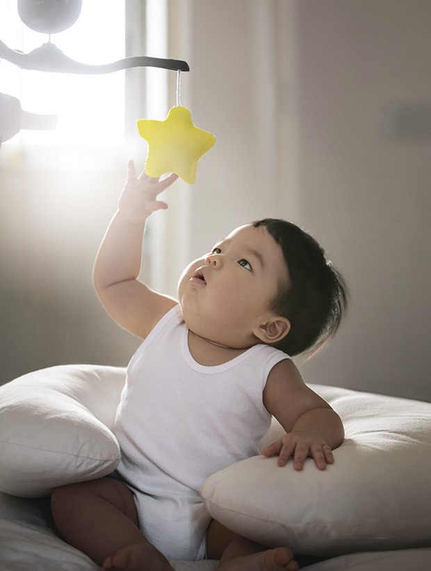 Asian toddler boy sitting on bed reaching out to catch a rotating toy star. Conceptual baby photo, "Reaching out to the star". (Foto: Getty Images)