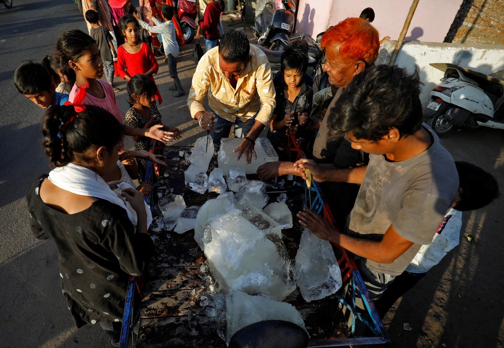 Homem quebra cubo de gelo para distribuir entre moradores de Ahmedabad, na Índia — Foto: Amit Dave/REUTERS