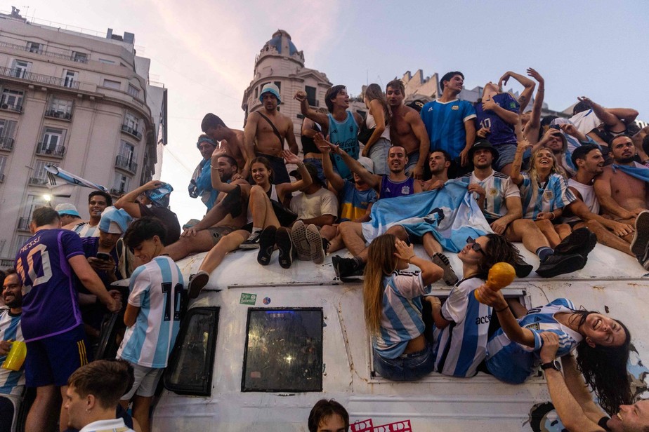 Torcedores argentinos sobem em carro para comemorar vitória na Copa do Mundo do Catar, em Buenos Aires