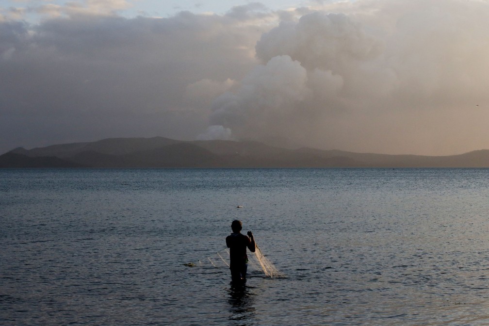 Homem pesca enquanto vulcão Taal segue em erupção nesta terça-feira (14)  — Foto: Eloisa Lopez/ Reuters