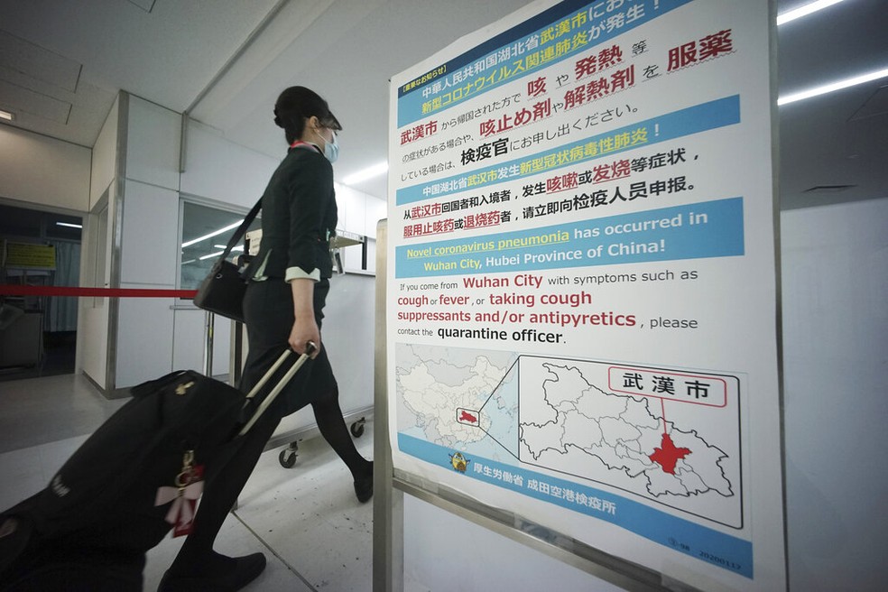 Uma comissária de bordo passa por scanners de temperatura corporal e um quadro de avisos sobre coronavírus no aeroporto internacional de Narita, perto de Tóquio, na quinta-feira (23) — Foto: Eugene Hoshiko/AP