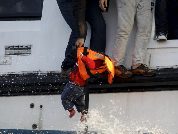 Um refugiado se prepara para entregar uma criança a um salva-vidas voluntário na ilha de Lesbos, na Grécia. O barco que eles estavam começou a afundar após atravessar o mar Egeu. Cerca de 150 imigrantes estavam a bordo, a maioria sírios. Não houve vítimas (Foto: Giorgos Moutafis/Reuters)