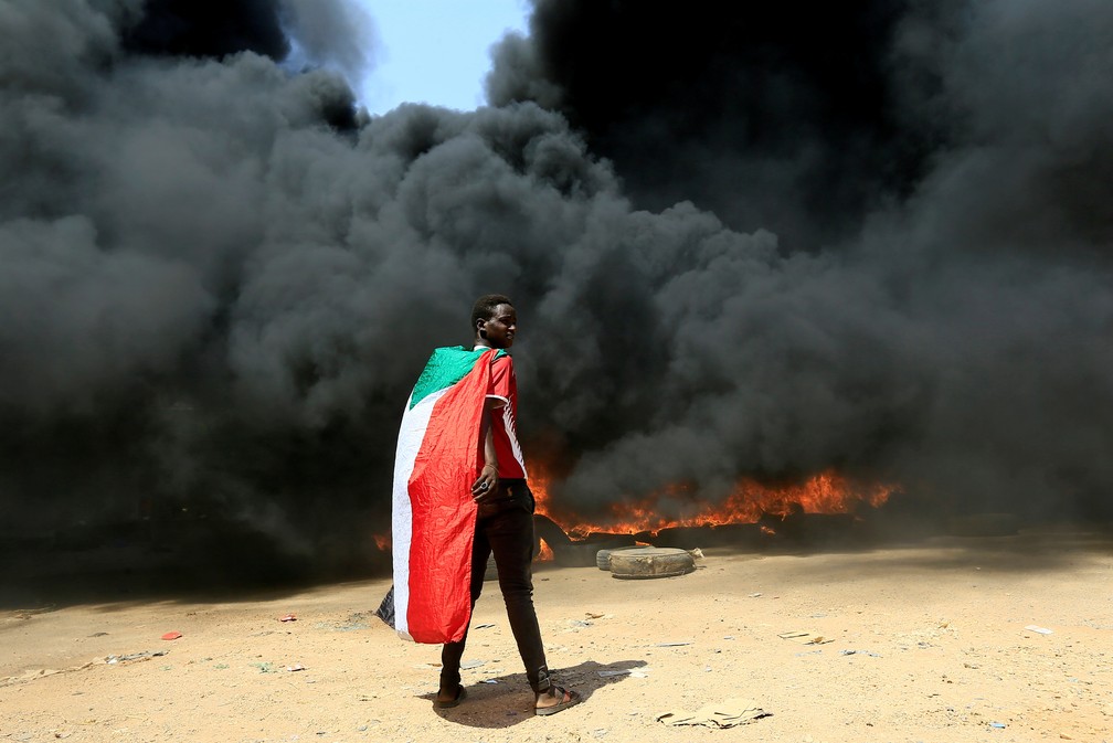 Manifestante exibe a bandeira do Sudão perto de uma barricada de pneus incendiada durante protesto na capital Cartum no dia 21 de outubro de 2021  — Foto: Mohamed Nureldin Abdallah/Reuters
