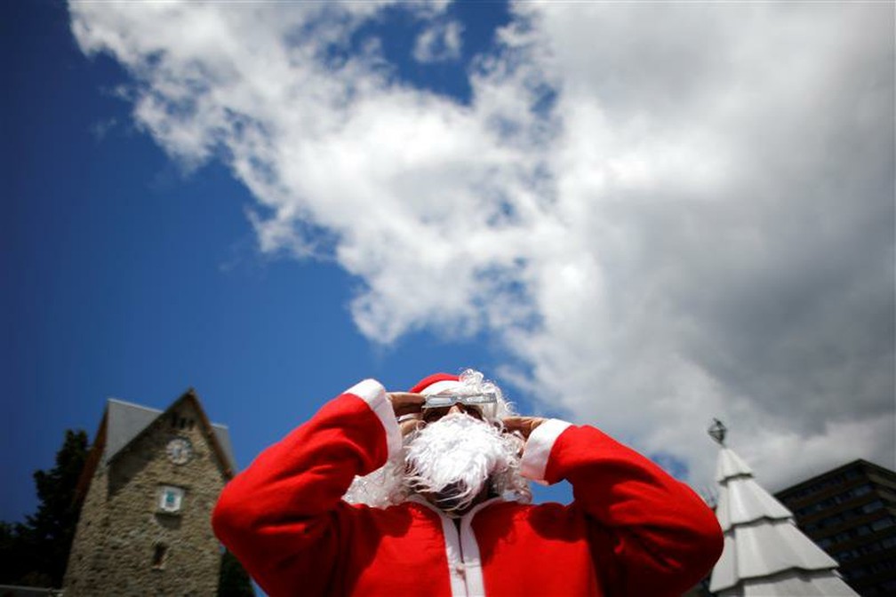 Homem vestido de Papai Noel usa óculos de proteção especiais para observar o eclipse nesta segunda-feira (14) em Bariloche, na Argentina. — Foto: Carlos Barria/Reuters