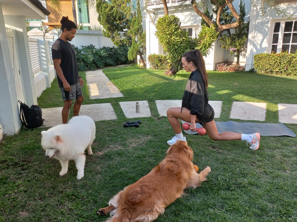 Rafa Kalimann faz o recuo alternado segurando halteres: observada por Zeus, seu personal trainer, e rodeada pelos c&atilde;es Troy e Alfredo &mdash; Foto: Eu atleta