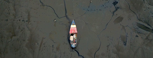 Barco de pesca encalhado em meio ao lodo acumulado na Praia de Sepetiba — Foto: Custodio Coimbra 