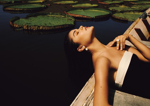 Nicole Correia Côrtes, modelo, deitada sobre canoa em meio á Vitórias-Régias, usa brinco e anel ambos de ouro de ágata, da nova coleção Água, de Carla Amorim. (Foto: Lufre/ Arquivo Vogue)
