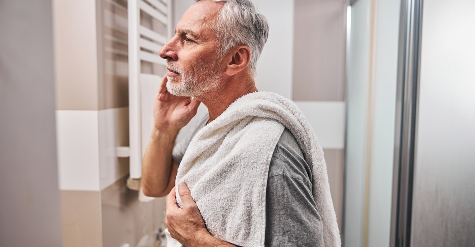Side-view photo of a serious aged man looking in the mirror while standing in the bathroom with a towel (Foto: Getty Images/iStockphoto)